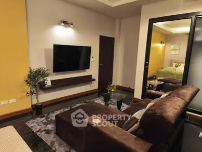Modern living room with cozy seating and wall-mounted TV next to a stylish bedroom.