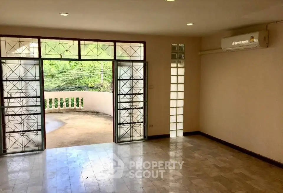 Spacious living room with large windows and balcony access, featuring natural light and modern flooring.