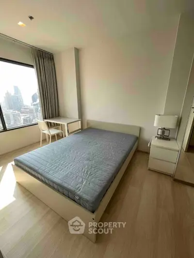 Modern bedroom with city view, featuring a sleek bed and stylish desk, perfect for urban living.