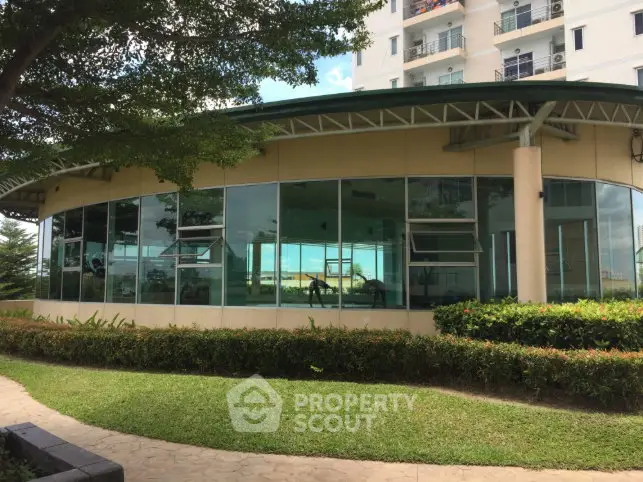 Modern gym with glass walls in a residential building, surrounded by lush greenery.