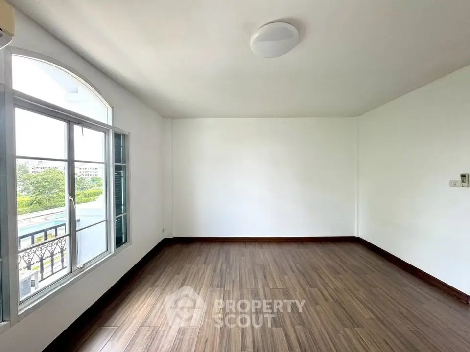 Spacious empty room with large window and wooden flooring, perfect for customization.