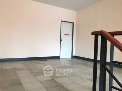 Spacious empty room with tiled flooring and a door, ideal for customization.
