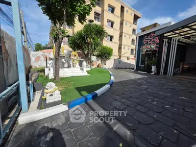 Charming garden entrance with lush greenery and paved pathway in urban setting.