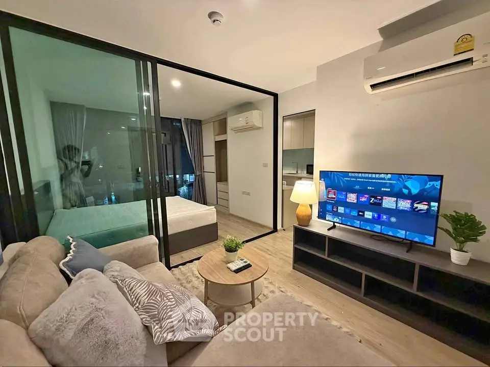 Modern living room with open layout, featuring a cozy sofa, flat-screen TV, and glass partition to bedroom.