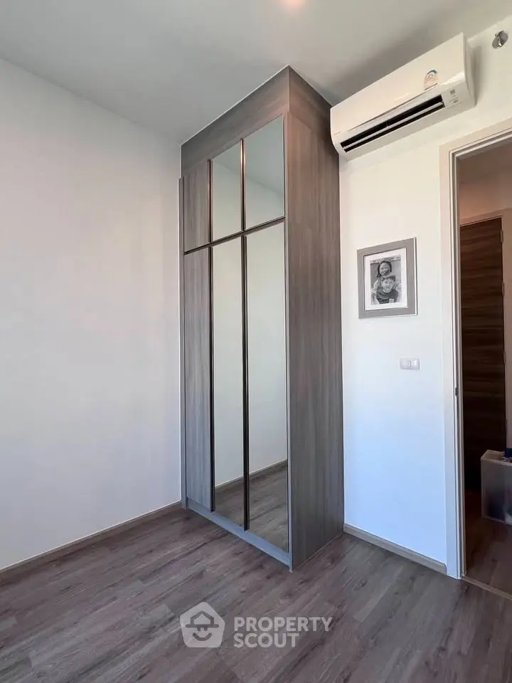 Modern bedroom with sleek mirrored wardrobe and air conditioning unit.