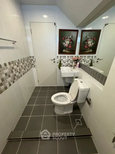 Modern bathroom with elegant tile design and floral artwork, featuring a sleek toilet and sink.