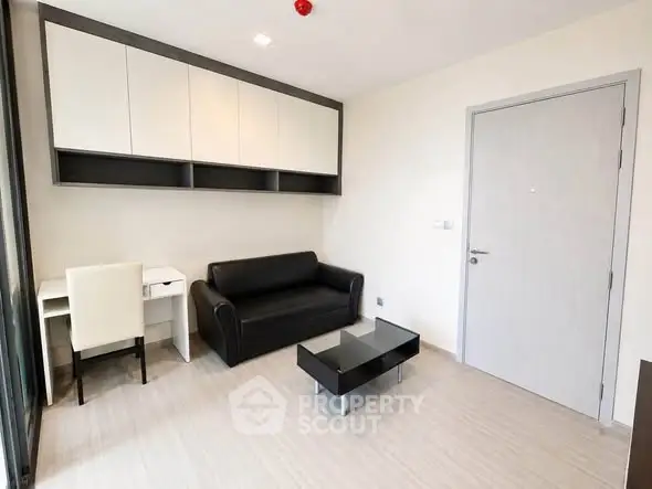 Modern living room with sleek black sofa, glass coffee table, and built-in storage cabinets.