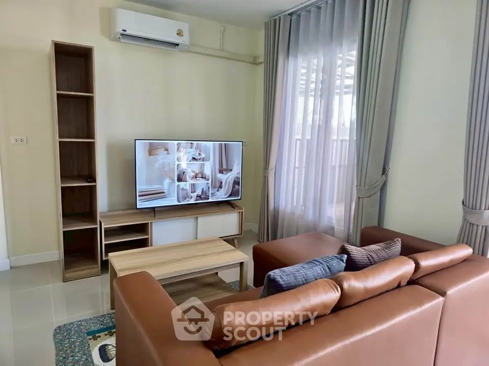 Modern living room with leather sofa, TV, and natural light from large windows.