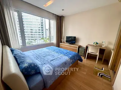 Modern bedroom with city view, featuring a cozy bed, desk, and large window in a high-rise apartment.