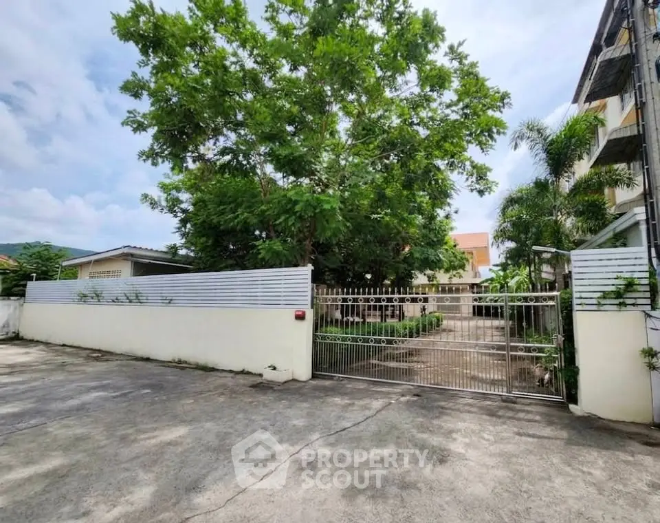 Spacious gated entrance with lush greenery and modern fencing in a serene neighborhood.