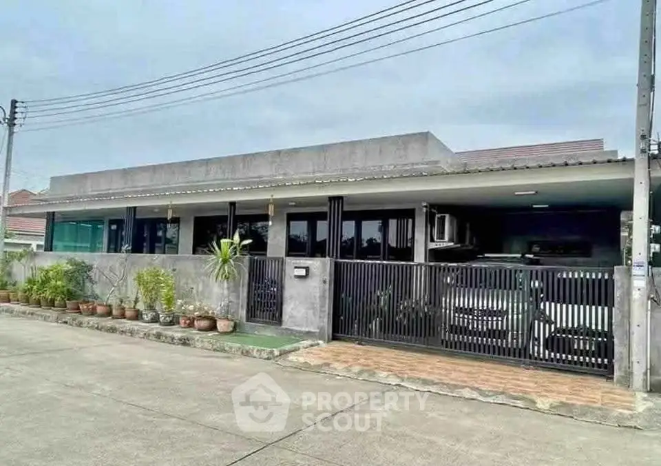 Modern single-story house with gated driveway and potted plants, showcasing contemporary architecture.