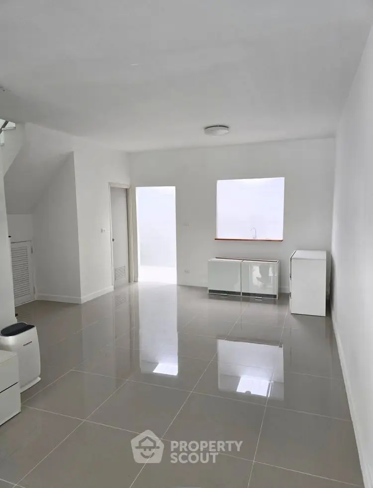 Spacious minimalist living room with glossy tiled floors and ample natural light.