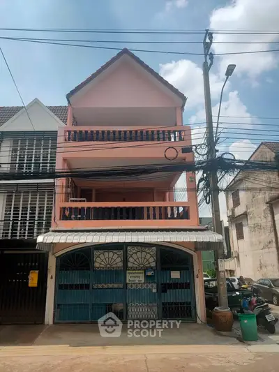 Charming three-story pink townhouse with balcony in urban setting.