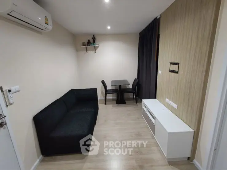 Modern living room with sleek black sofa and dining area, featuring minimalist decor and neutral tones.