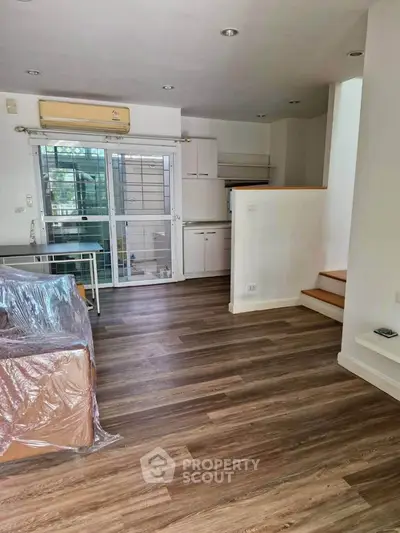 Modern living room with wooden flooring and open kitchen layout in a stylish apartment.
