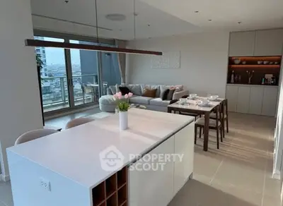 Modern open-plan living room with kitchen and balcony view, featuring elegant decor and natural light.