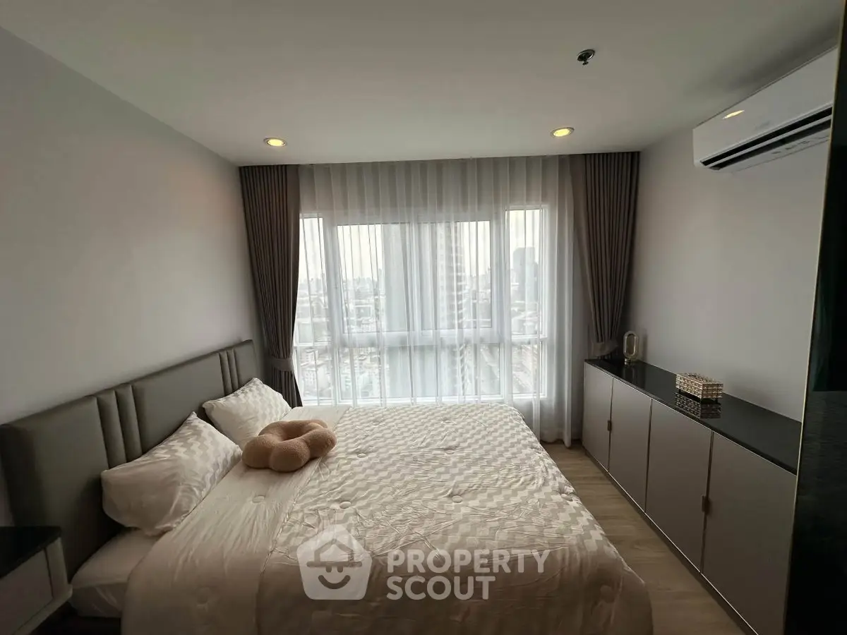 Modern bedroom with large window and city view, featuring a comfortable bed and sleek air conditioning unit.