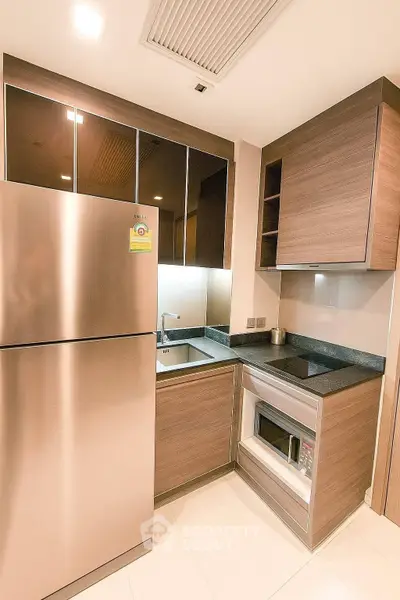 Modern kitchen with sleek appliances and wooden cabinetry, featuring a stainless steel fridge and built-in microwave.