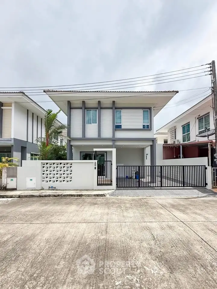 Modern two-story house with sleek design and gated entrance in a suburban neighborhood.