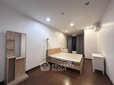 Spacious bedroom with wooden flooring and modern furniture in a well-lit apartment.