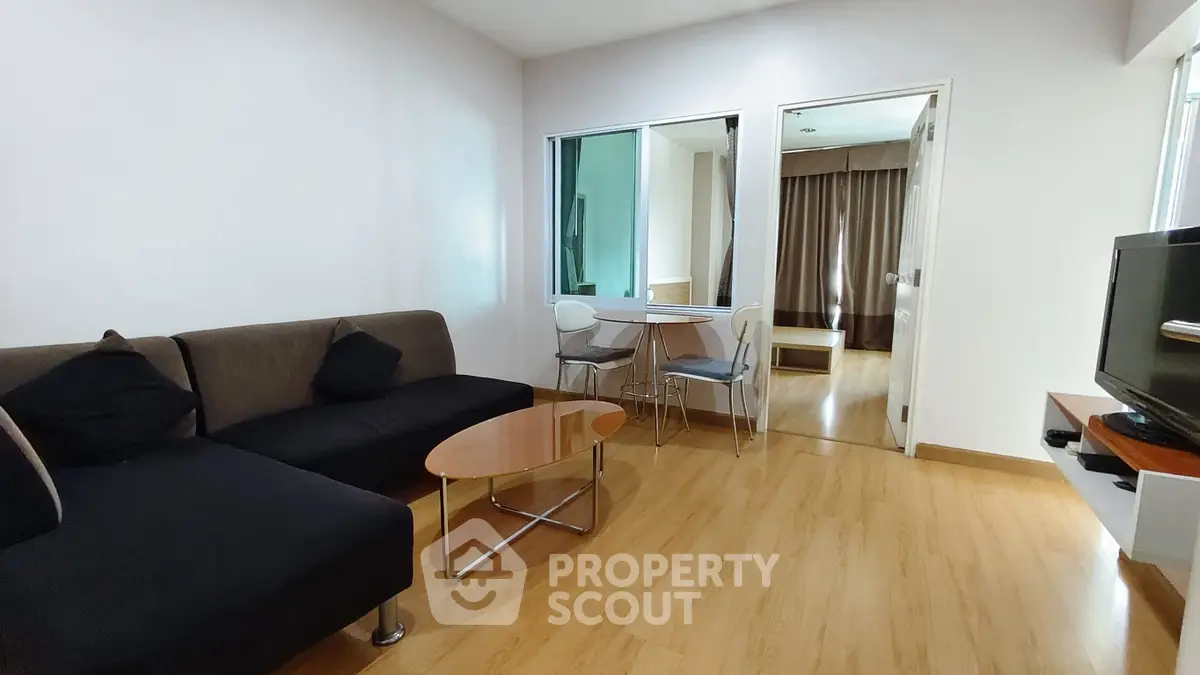 Modern living room with sleek furniture and wooden flooring, connecting to a cozy bedroom.