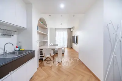 Modern open-plan living room with sleek kitchen and dining area, featuring elegant wood flooring and natural light.