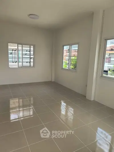 Spacious empty room with tiled flooring and large windows offering natural light.