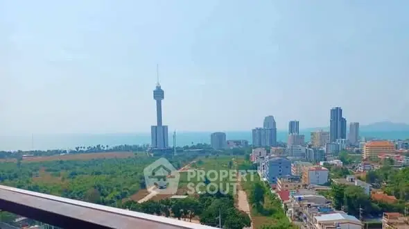 Stunning cityscape view from a high-rise balcony overlooking lush greenery and ocean horizon.