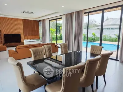 Luxurious open-plan living and dining area with pool view, featuring elegant furniture and floor-to-ceiling windows.