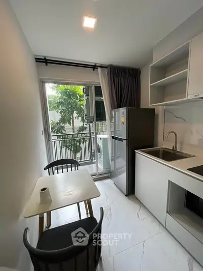 Modern kitchen with sleek design, featuring a compact dining area and a view of the balcony.