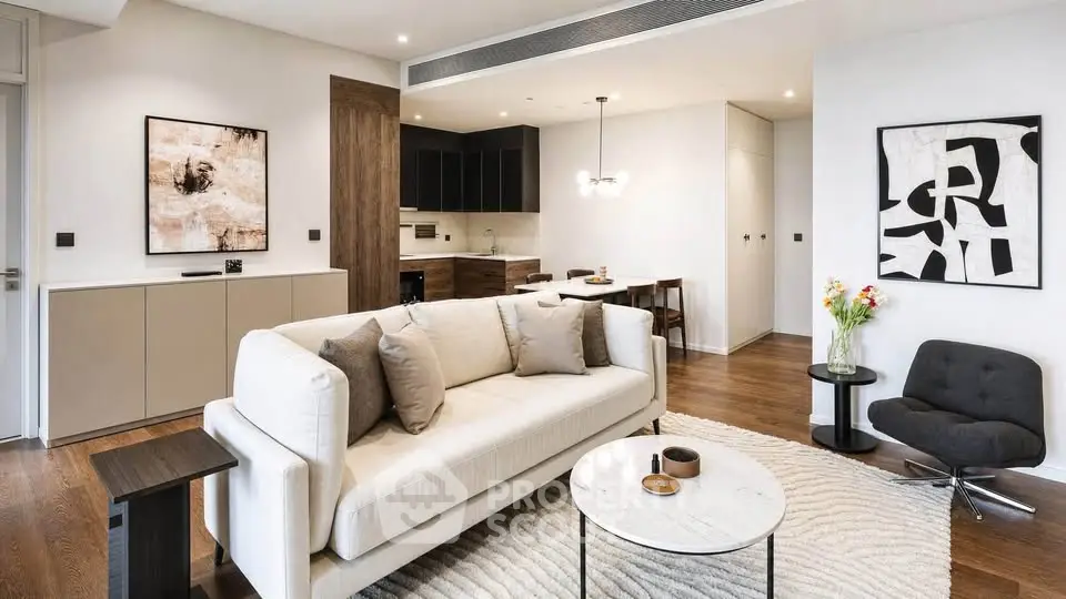 Modern living room with stylish decor and open kitchen layout, featuring elegant furniture and contemporary artwork.