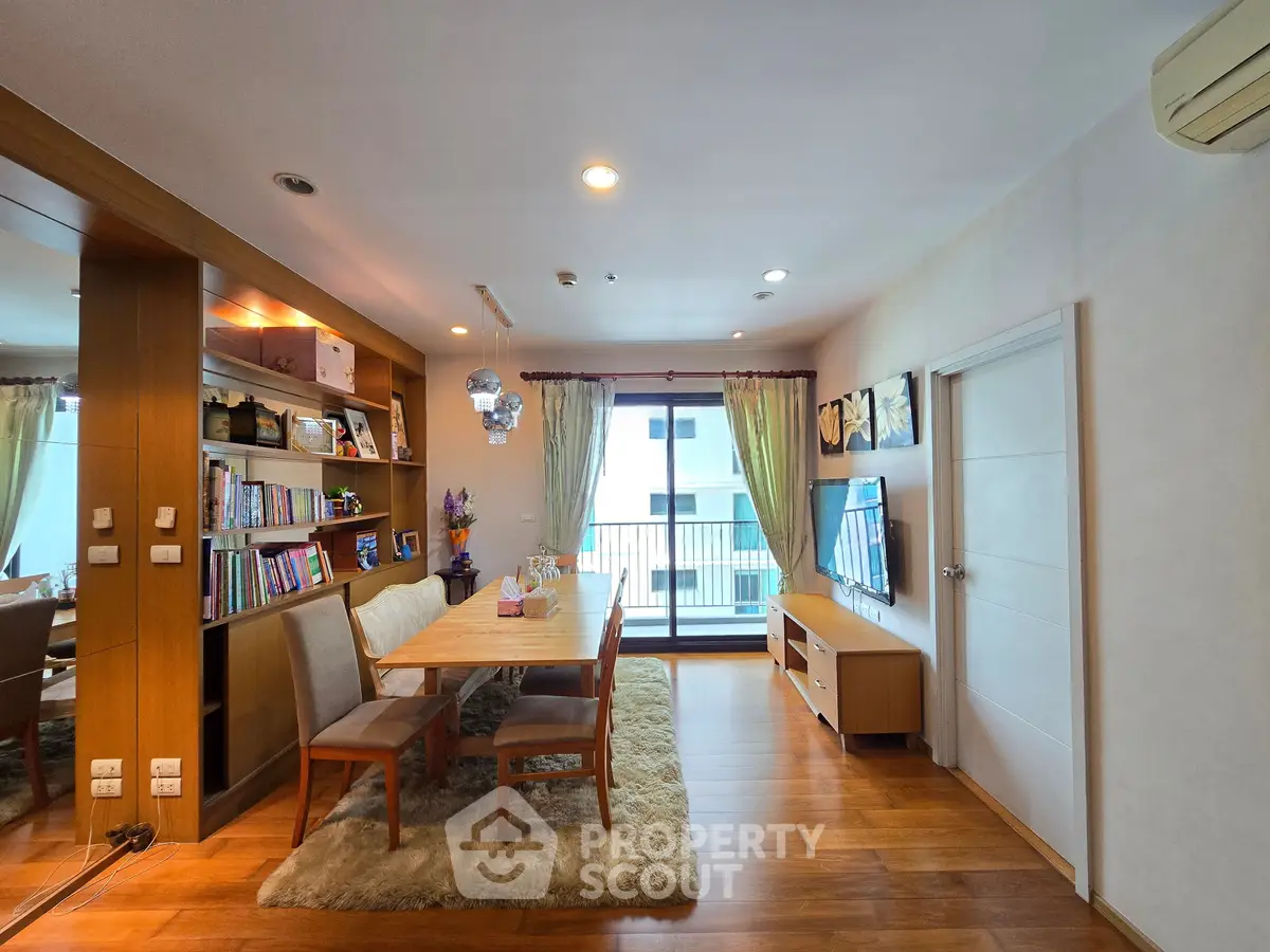 Spacious living room with elegant dining area and balcony access, featuring wooden flooring and modern decor.