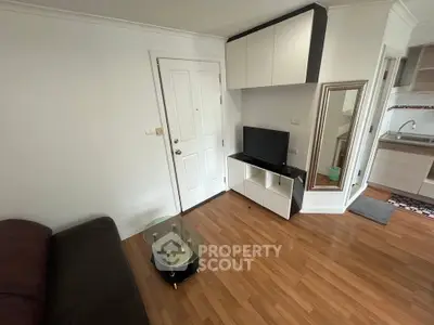 Cozy living room with modern furniture and wooden flooring, adjacent to a compact kitchen area.