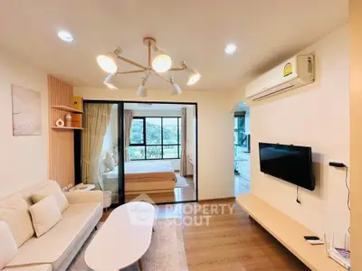 Modern living room with stylish decor and open view to bedroom, featuring sleek furniture and natural light.