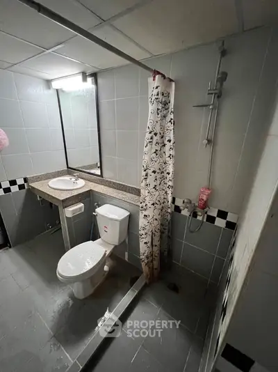 Compact bathroom with full tiling, shower area, toilet, and sink with storage space, ideal for efficient living in urban homes.