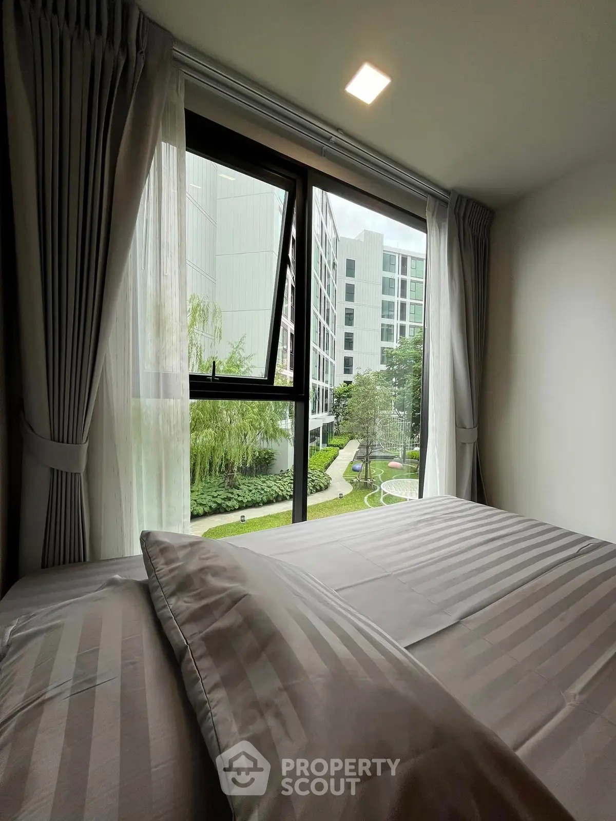 Cozy bedroom with large window offering a serene garden view in modern apartment.