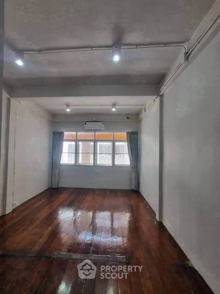Spacious empty room with polished wooden floors and large windows, ideal for customization.