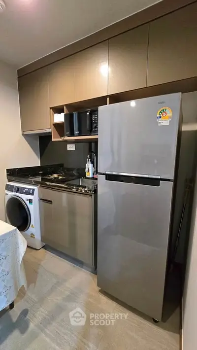Modern kitchen with sleek appliances including fridge and washing machine, compact yet functional design.