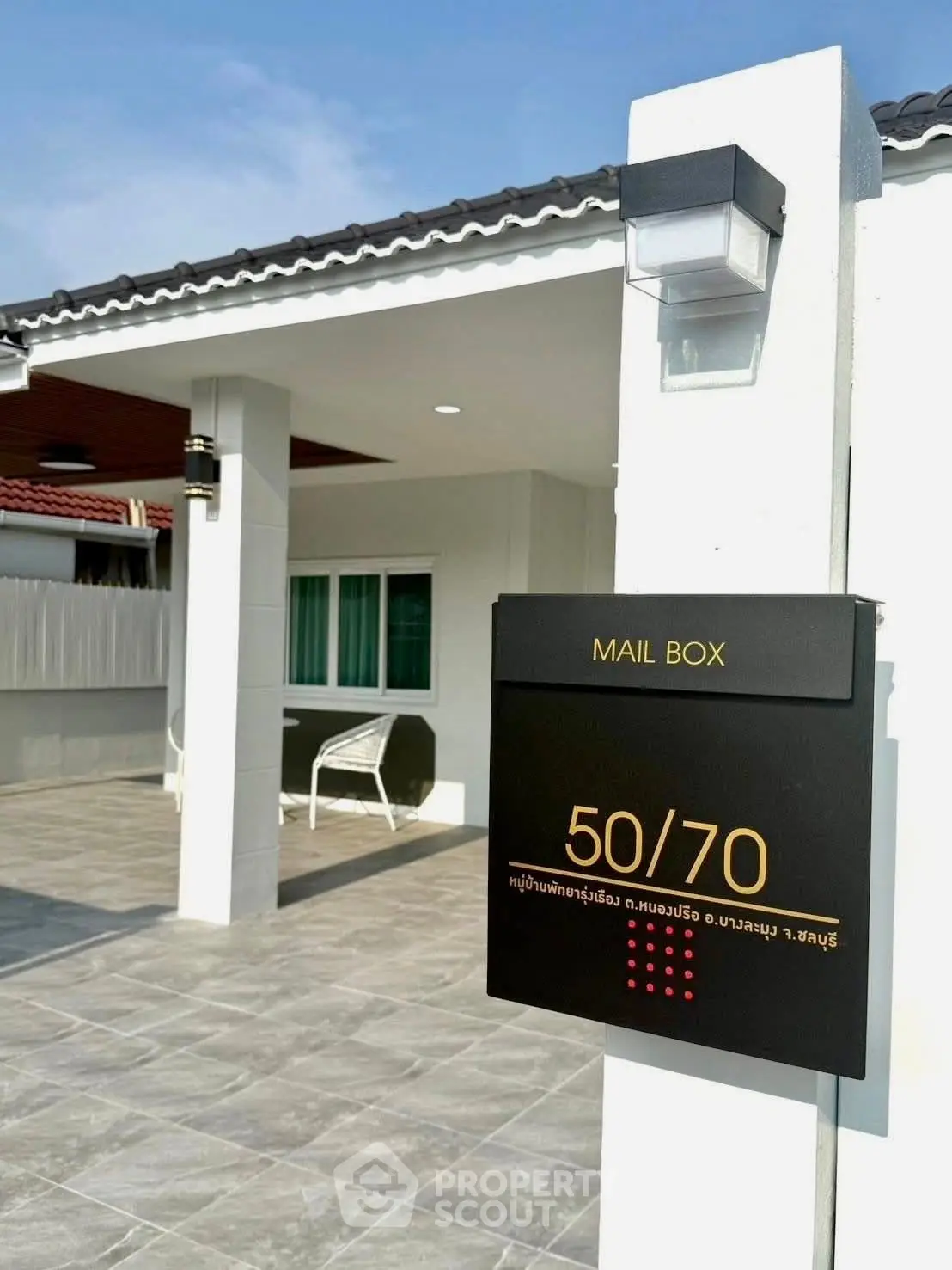 Modern house exterior with mailbox and tiled patio in sunny setting.