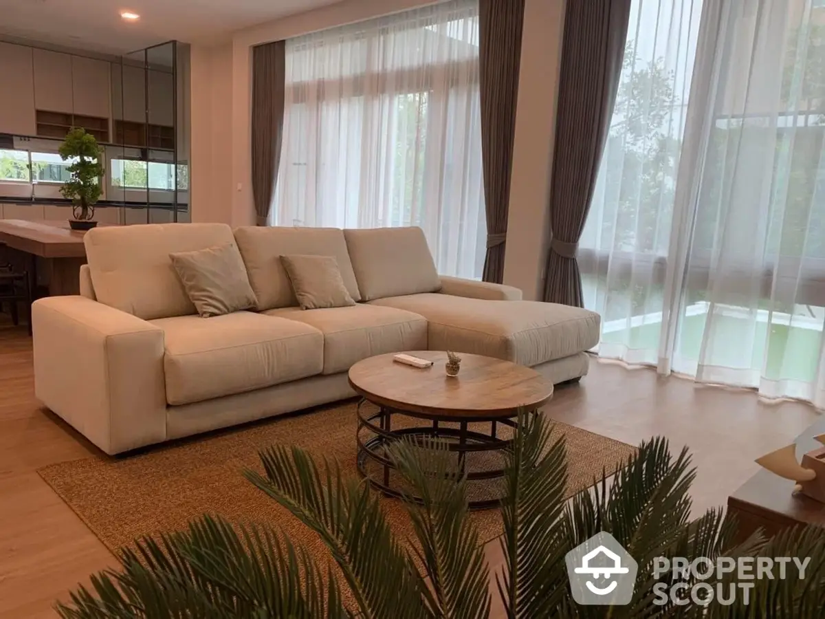 Spacious and elegant living room with a plush white sectional sofa, modern coffee table, and floor-to-ceiling sheer curtains allowing natural light to enhance the serene ambiance.