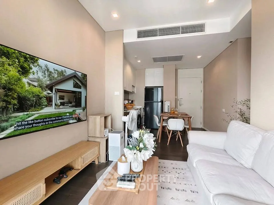 Modern living room with cozy seating and large TV, open to dining area and kitchen with sleek appliances.