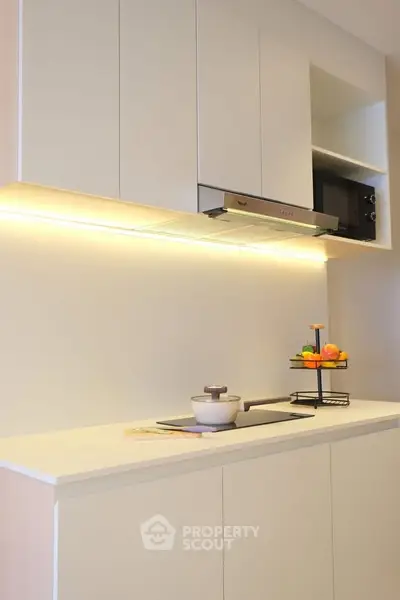 Modern kitchen with sleek cabinetry and under-cabinet lighting, featuring a compact stovetop and built-in microwave.