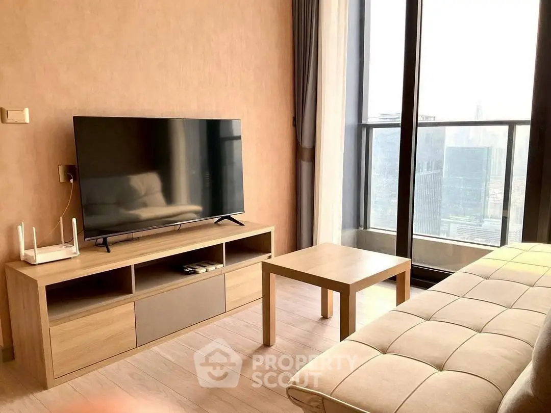 Modern living room with large TV and city view from balcony, featuring stylish furniture and natural light.
