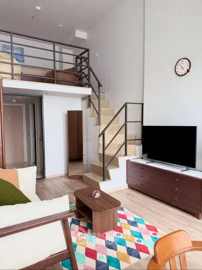 Modern loft-style living room with mezzanine, colorful rug, and sleek furniture.