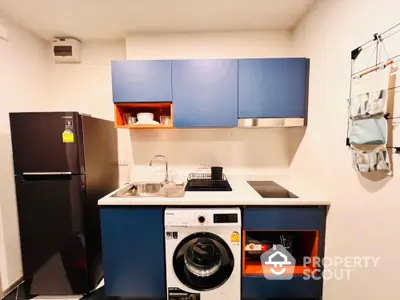 Modern compact kitchen with blue cabinets, washing machine, and sleek appliances.