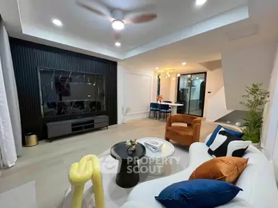 Modern living room with stylish decor, featuring a large TV, cozy seating, and elegant lighting.