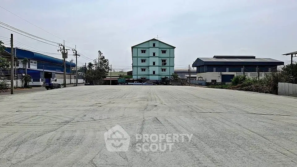 Spacious vacant lot with potential for development, surrounded by industrial buildings and clear sky.