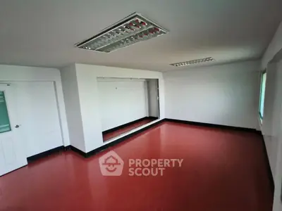 Spacious empty room with red flooring and large mirror, ideal for creative studio or office space.