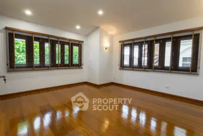 Spacious empty room with polished wooden floors and large windows offering natural light.