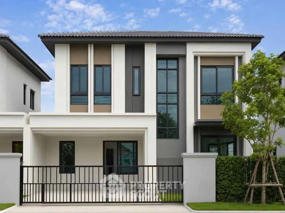 Modern two-story house with sleek design and gated entrance, featuring large windows and a manicured lawn.